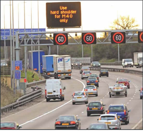Figure 20. Photo of cars on roadway with overhead sign reading "Use hard shoulder for M40 only."